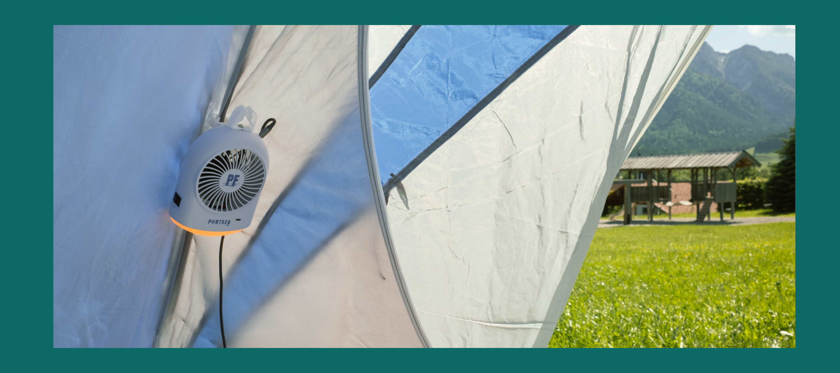 Portable fan attached to a tent with a scenic background of mountains and a building.